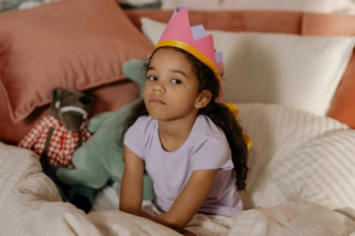 unhappy girl wearing paper crown sitting on bed