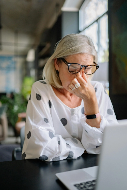 Stressed older woman rubbing her eyes while using a laptop.