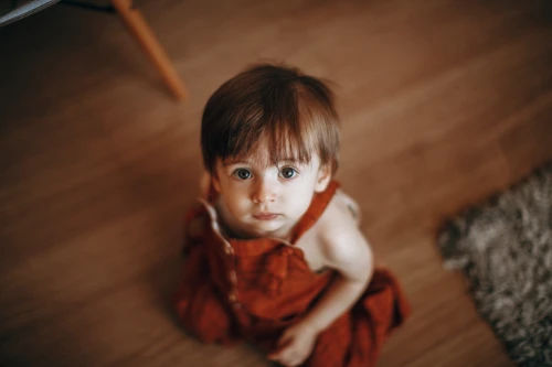 A toddler in orange overalls looking up at camera.