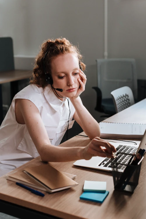 Woman with headset looking bored at an office desk.