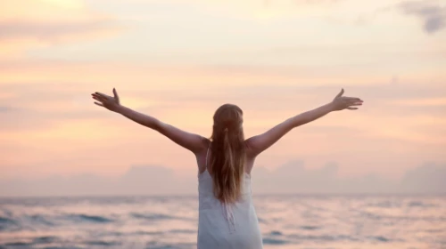 woman with arms outstretched on beach at sunset