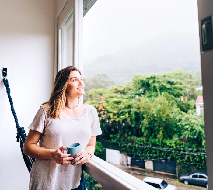 woman with mug standing looking out of open window.