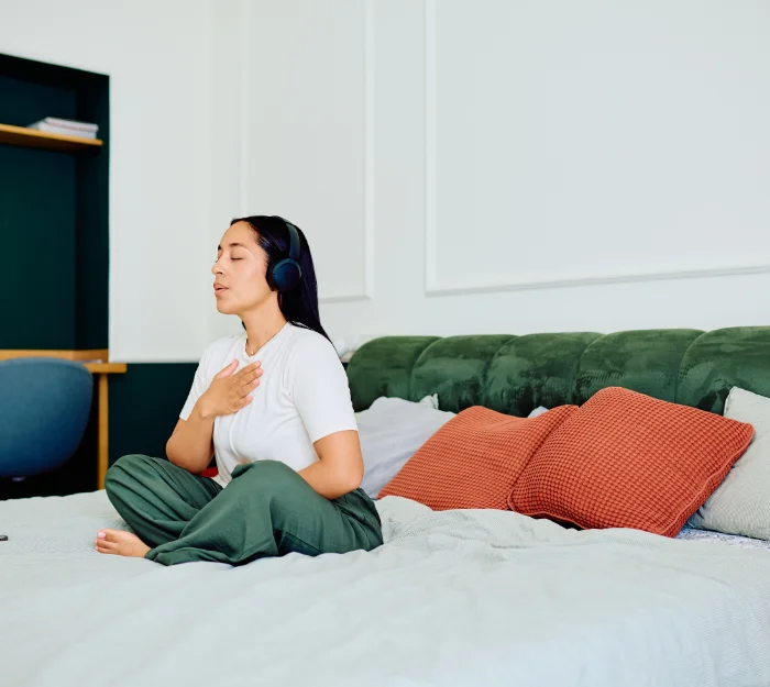 woman with headphones sitting on bed meditating