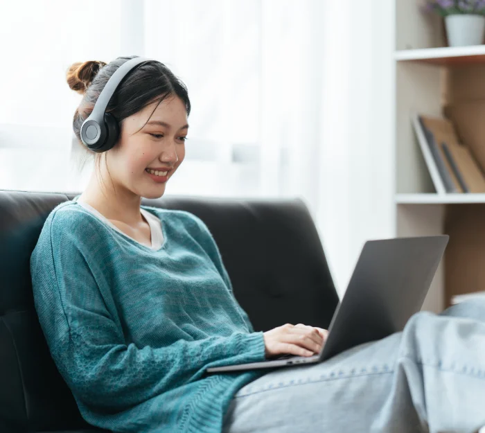 smiling woman with headphones sitting on sofa looking at laptop screen